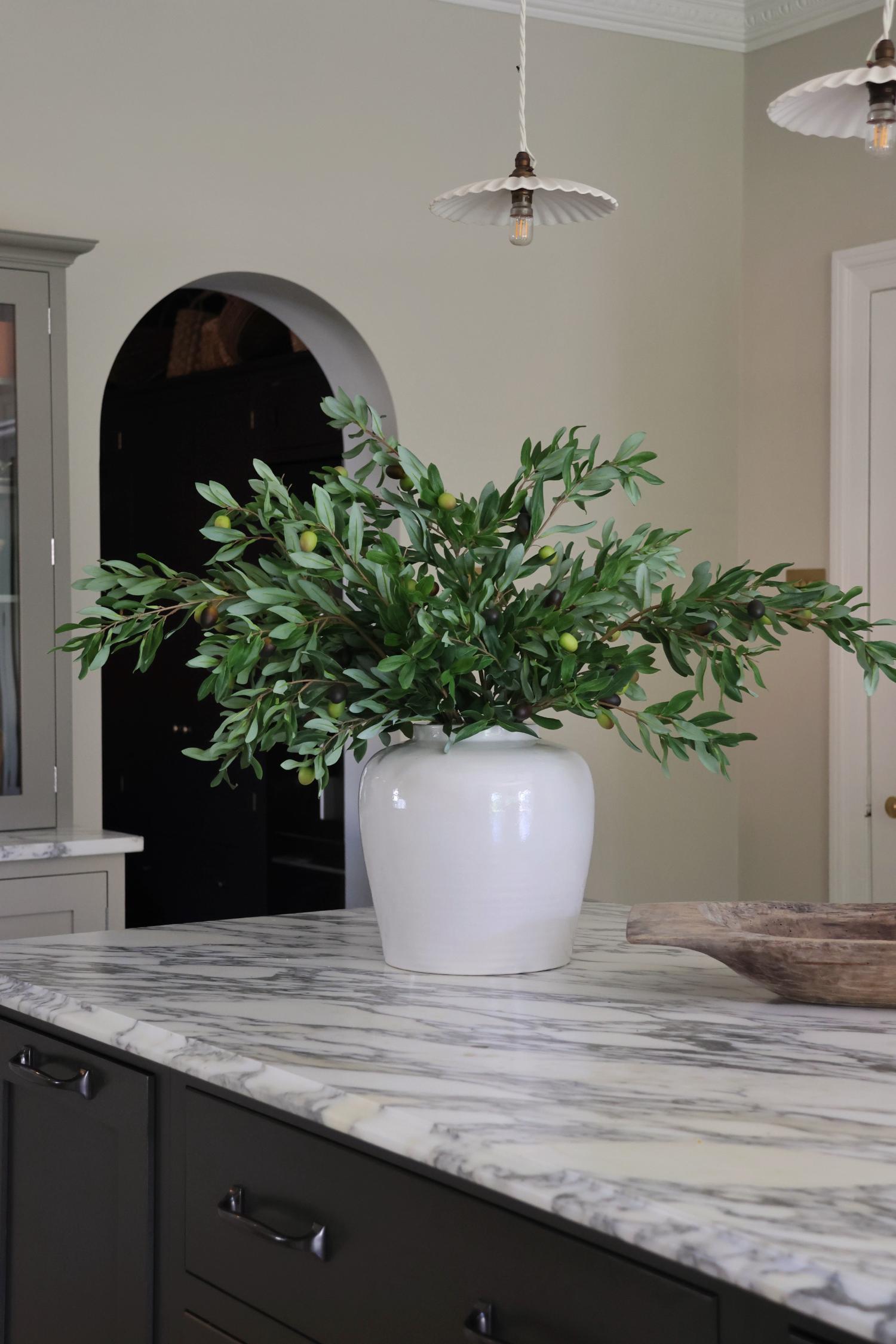 large white vase with olive stems on marble worktop in kitchen