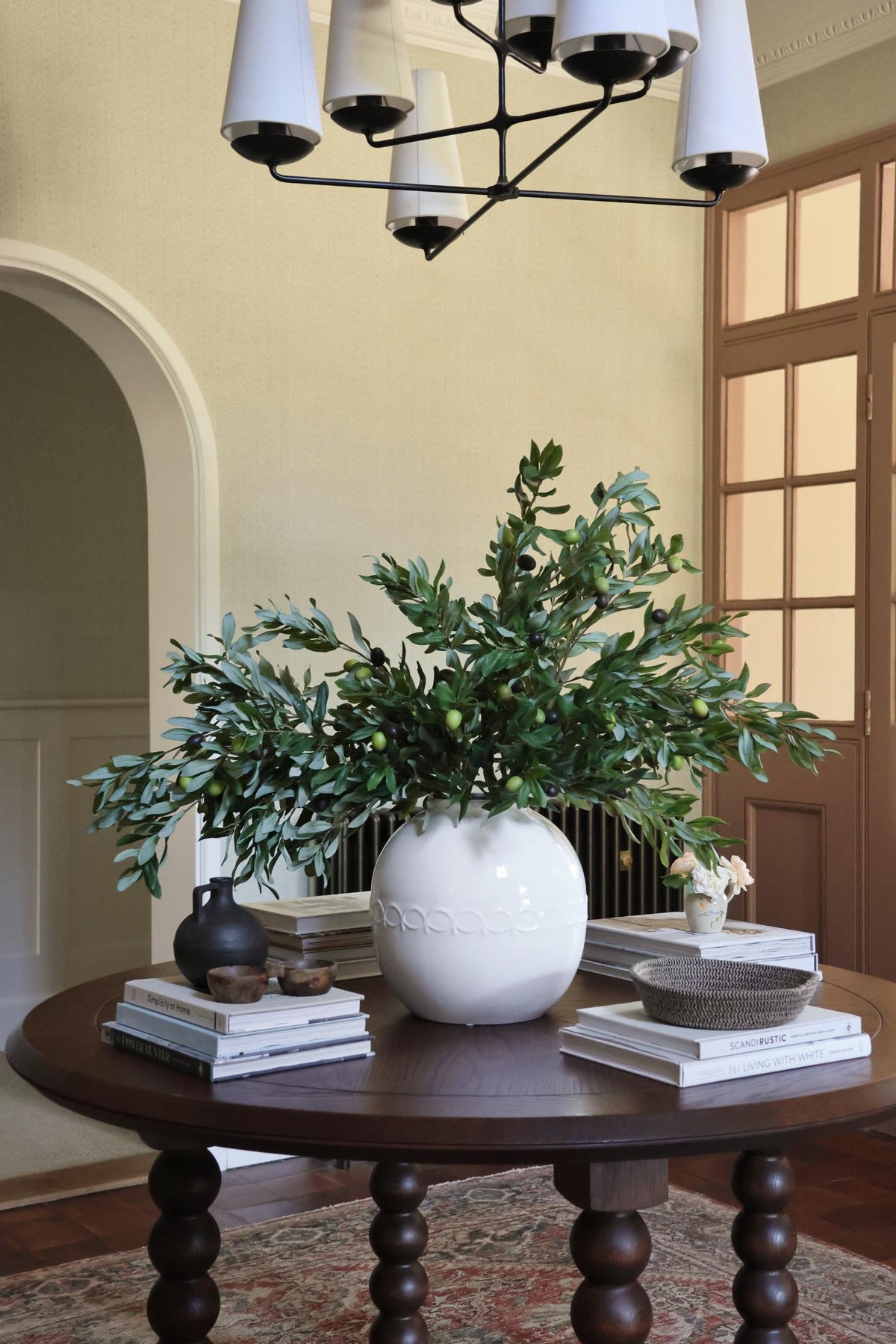 white vase of olive stems on large wooden round table