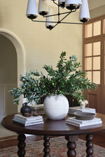 white vase of olive stems on large wooden round table