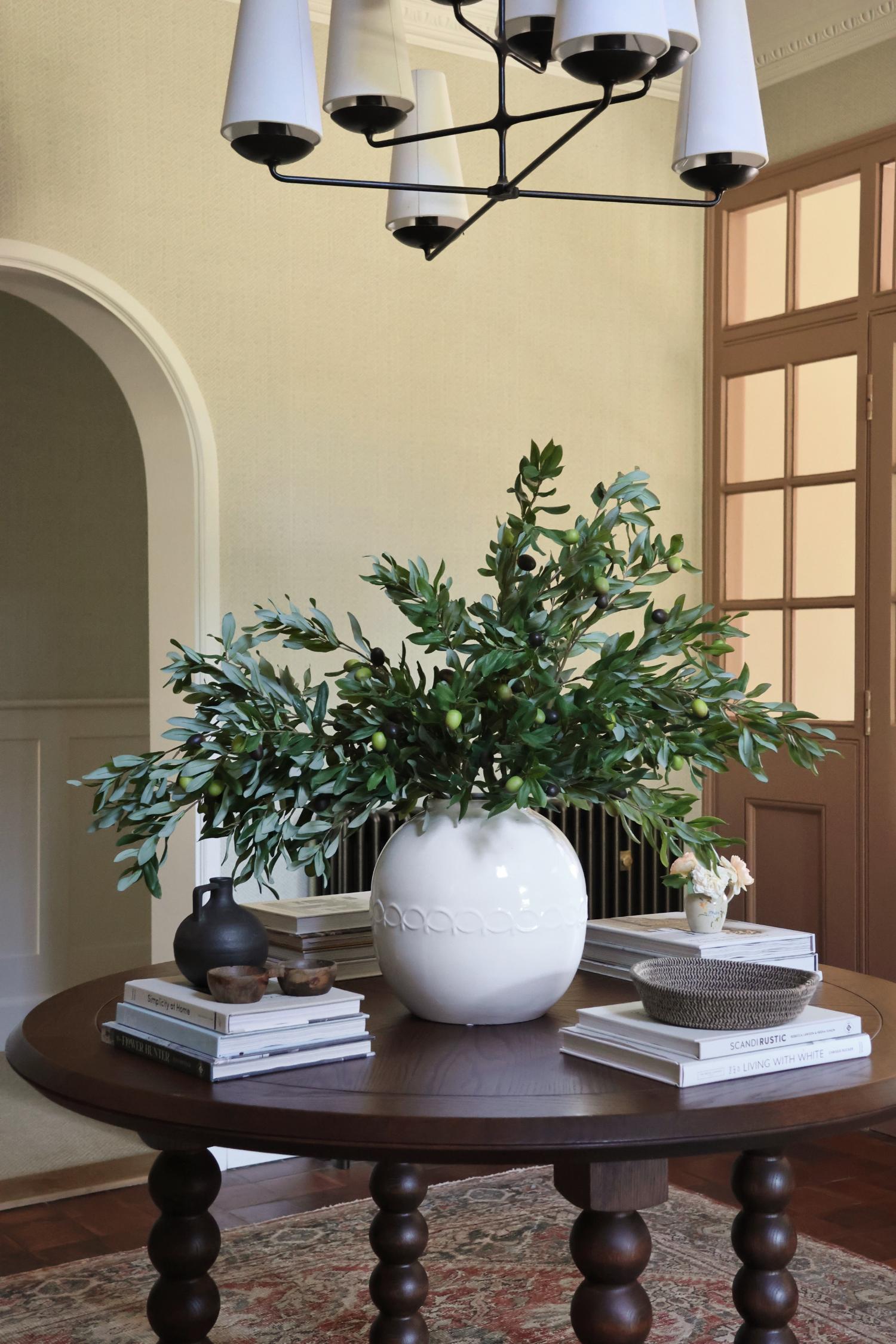 white vase of olive stems on large wooden round table