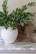 rustic white vase with faux olive branches on a marble worktop