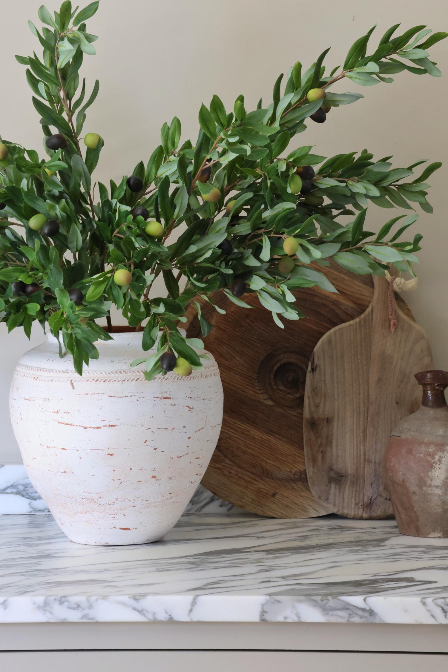 rustic white vase with faux olive branches on a marble worktop