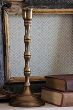 Bronze candlestick on a surface with books and a textured wall in the background