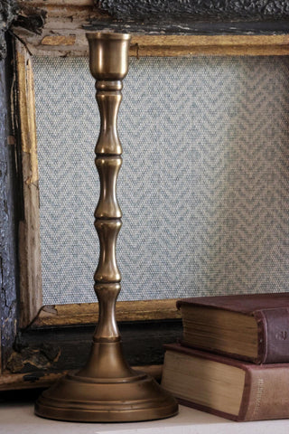 Bronze candlestick on a surface with books and a textured wall in the background