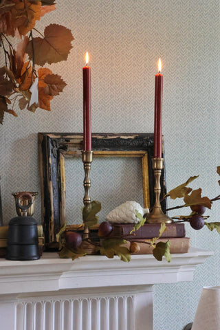 Decorative setup with candles, leaves, and a framed picture on a mantelpiece.