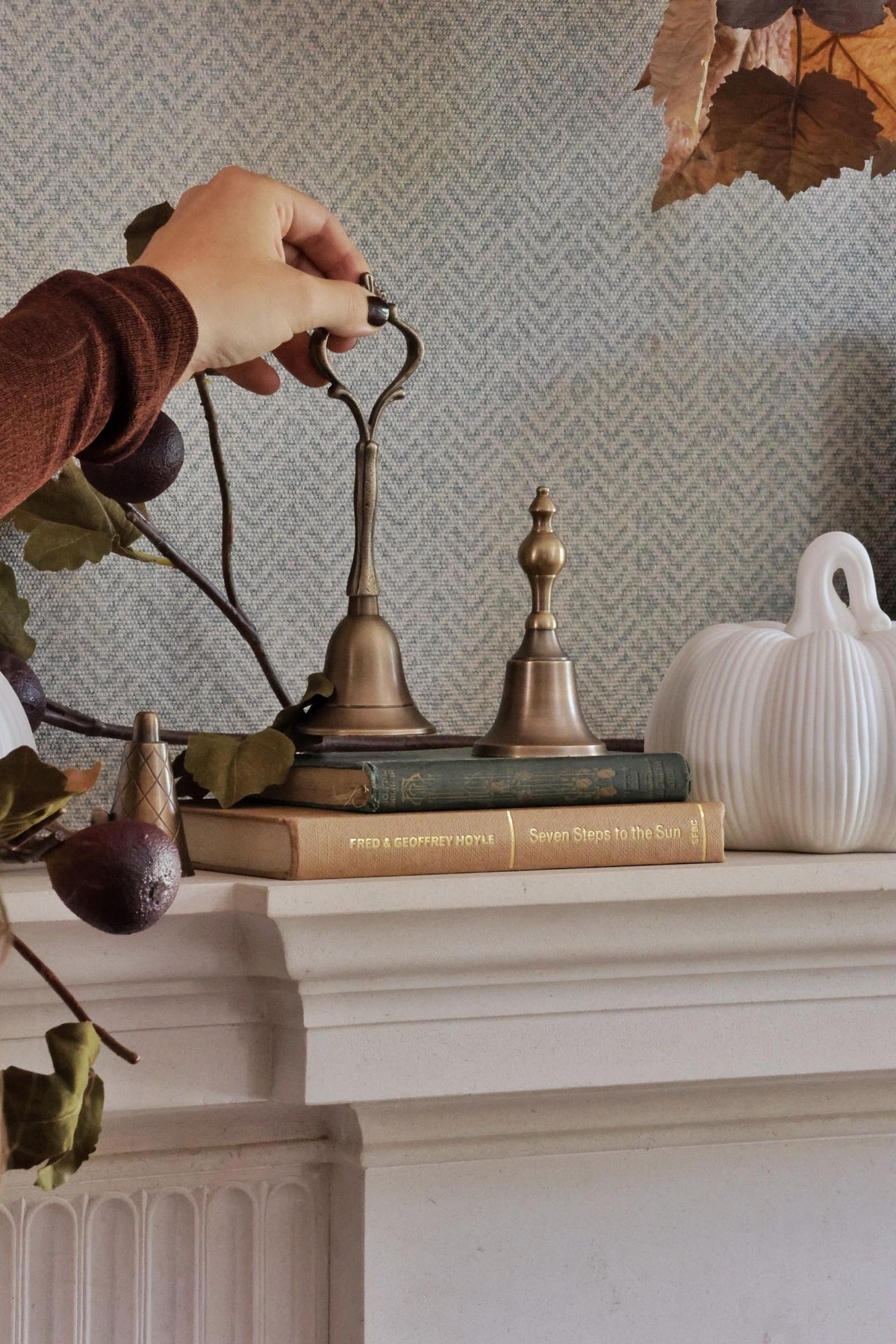 Decorative items on a mantelpiece with a hand reaching for a bell.