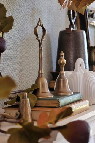 Decorative arrangement with brass candlesticks, books, and leaves on a textured surface.