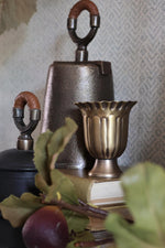 Decorative items including a metallic bell, urn, and books on a textured surface.