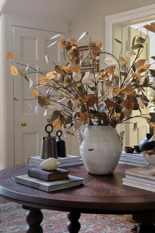 Decorative vase with autumn leaves on a wooden table in a room.