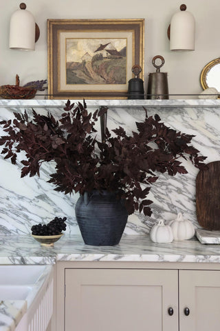 Decorative setup with a vase of dark artificial cimicfuga on a marble surface, framed artwork, and decorative items.