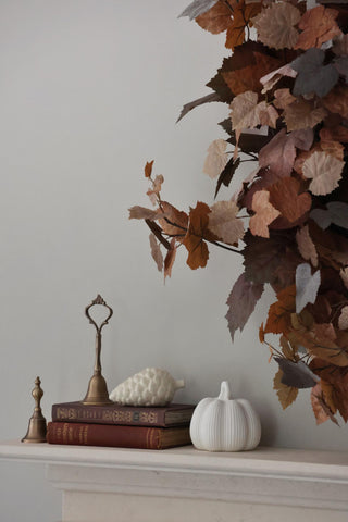 Decorative setup with fall leaves, books, and a pumpkin on a mantelpiece against a neutral wall.