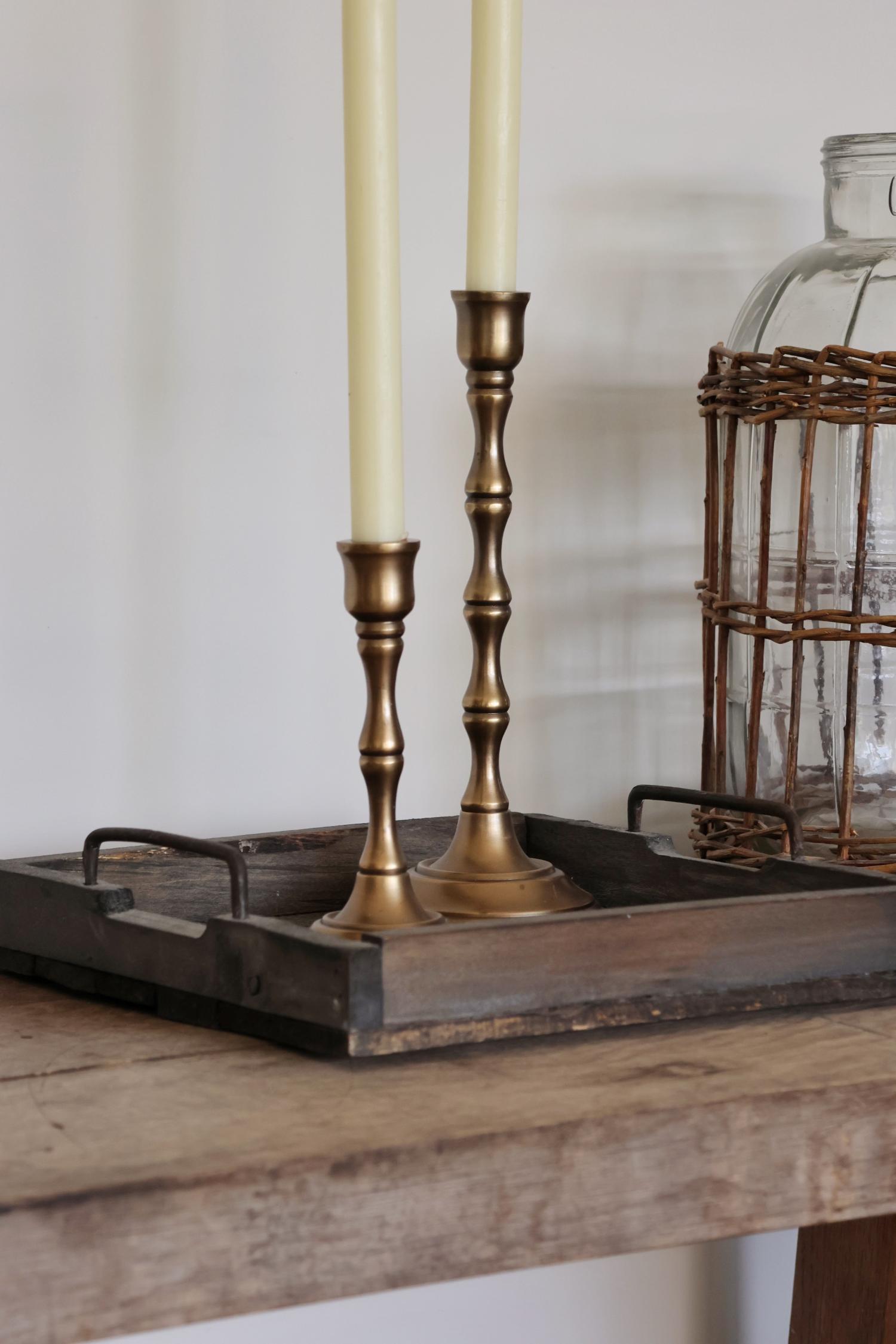 two brass candlesticks with candles on a wooden surface