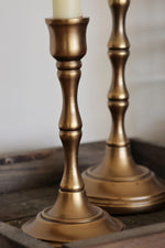 Two brass candle holders on a wooden surface with a neutral background