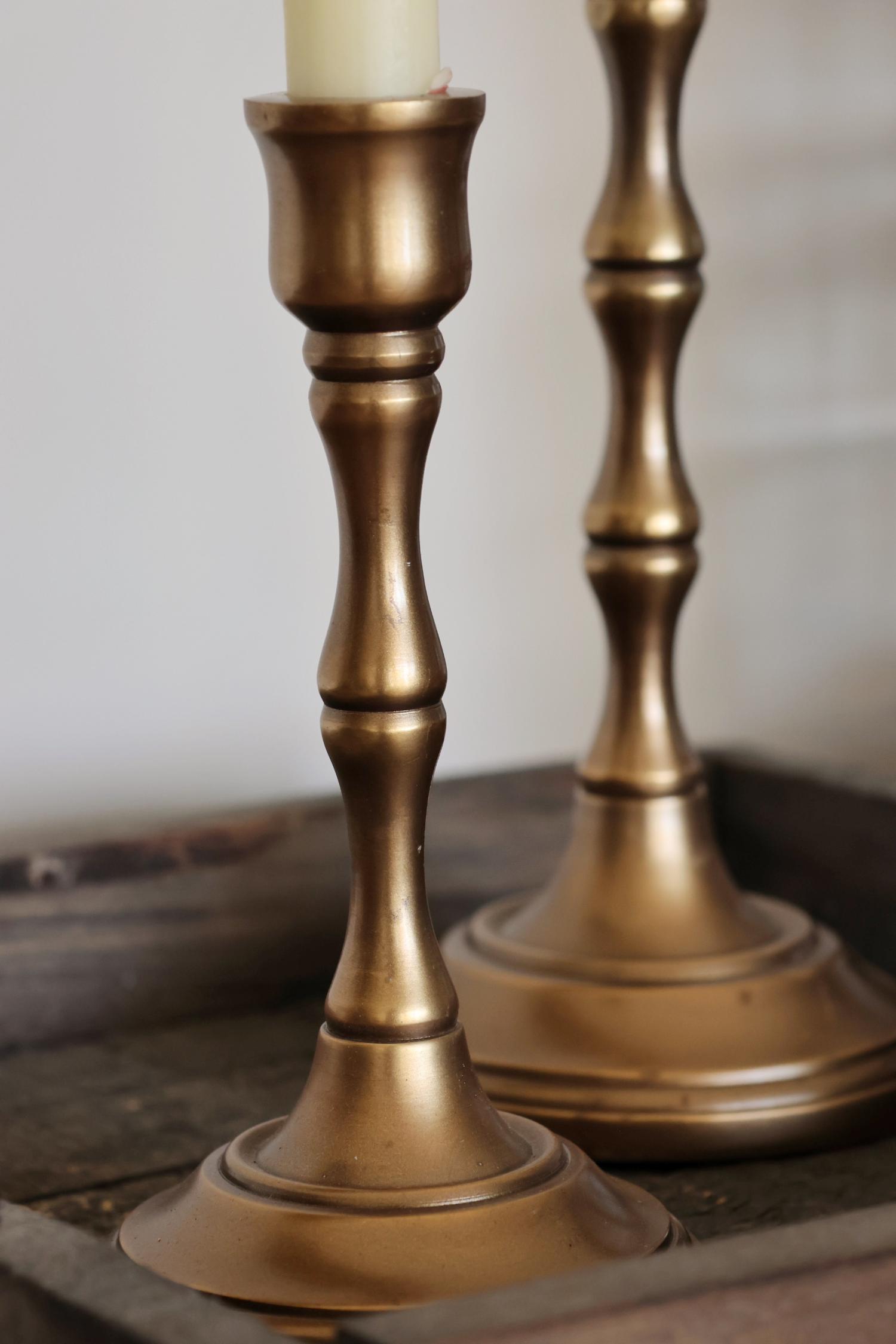 Two brass candle holders on a wooden surface with a neutral background