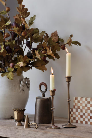 Decorative setting with candles, a vase of leaves, and rustic objects on a wooden surface.