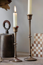 Two brass candle holders with candles on a wooden surface against a gray background