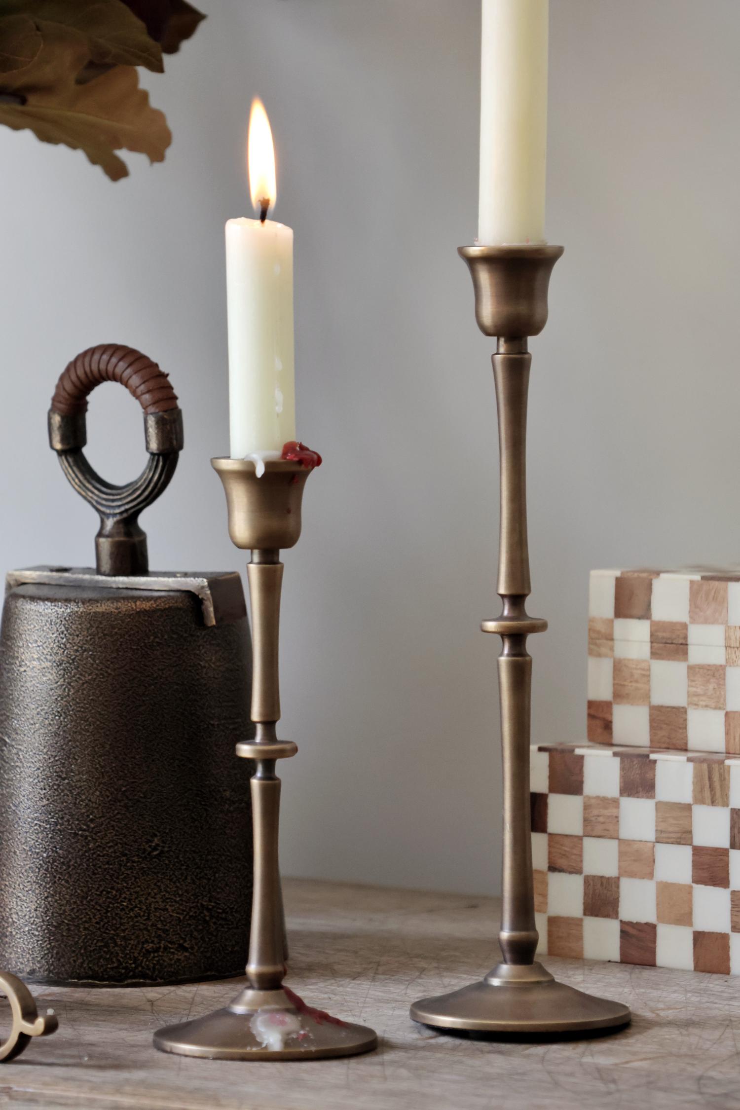 Two brass candle holders with candles on a wooden surface against a gray background