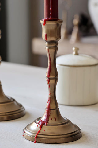 Brass candlestick with a red candle that has melted wax dripping down.