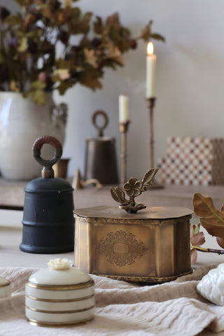 Decorative items including a black bell, gold box, and white container on a table with a blurred background.