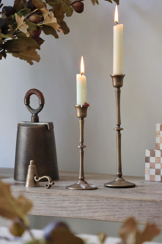Decorative candlesticks with candles on a wooden surface, surrounded by foliage and small decorative items.