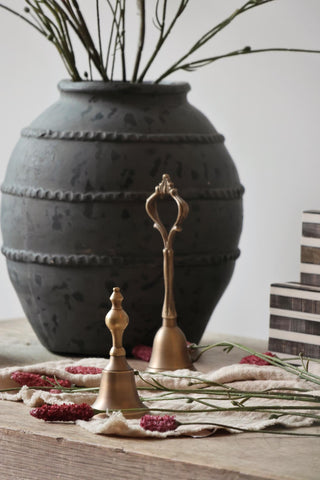 Decorative scene with a large black vase, gold bell, and small books on a wooden surface.