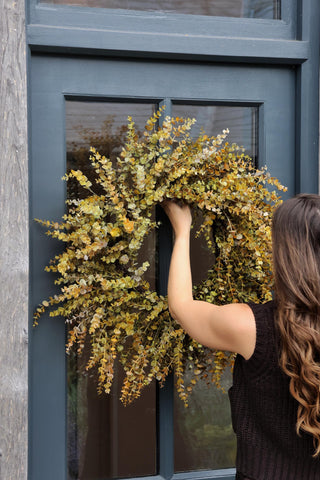 Person hanging a floral autumn wreath on a door