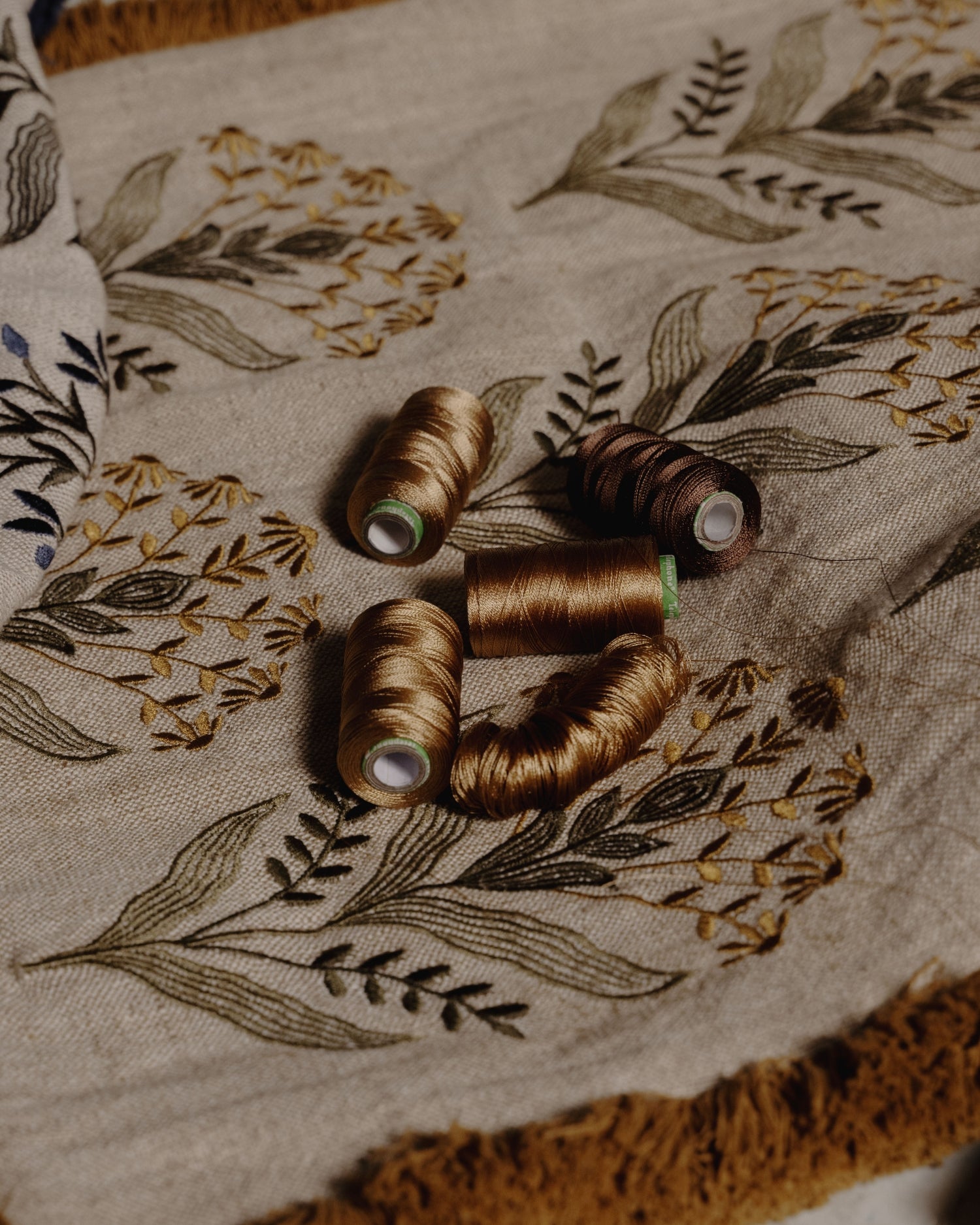 Spools of brown and mustard thread on a fabric with floral embroidery