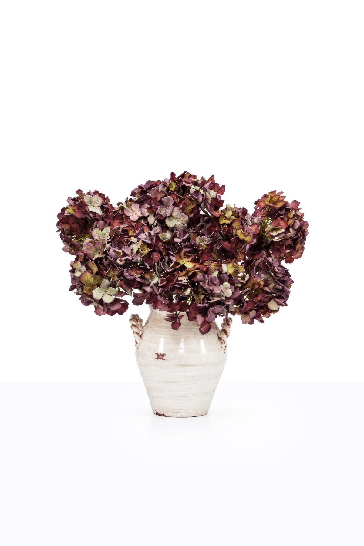 A bouquet of artificial mulberry hydrangeas in a ceramic vase in a white studio