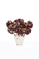 A bouquet of artificial mulberry hydrangeas in a ceramic vase in a white studio