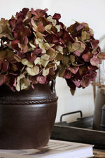 Decorative brown pot with artificial burgundy  dried hydrangeas on a surface