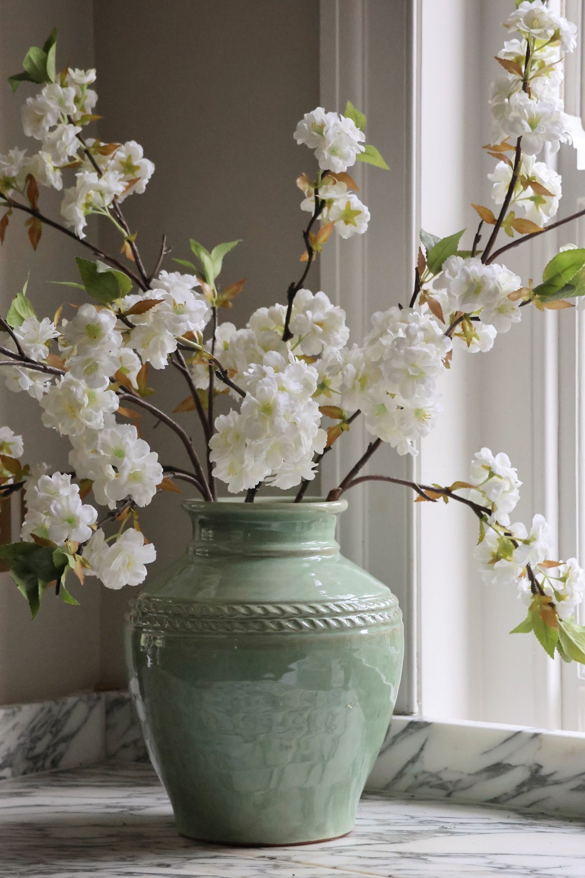 Green vase with white flowers on a marble surface
