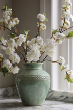 Green vase with white flowers on a marble surface
