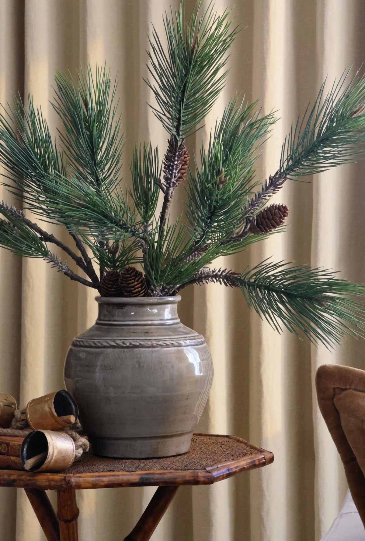 Grey rustice ceramic vase with artificial green foliage in on a bamboo table with plain background