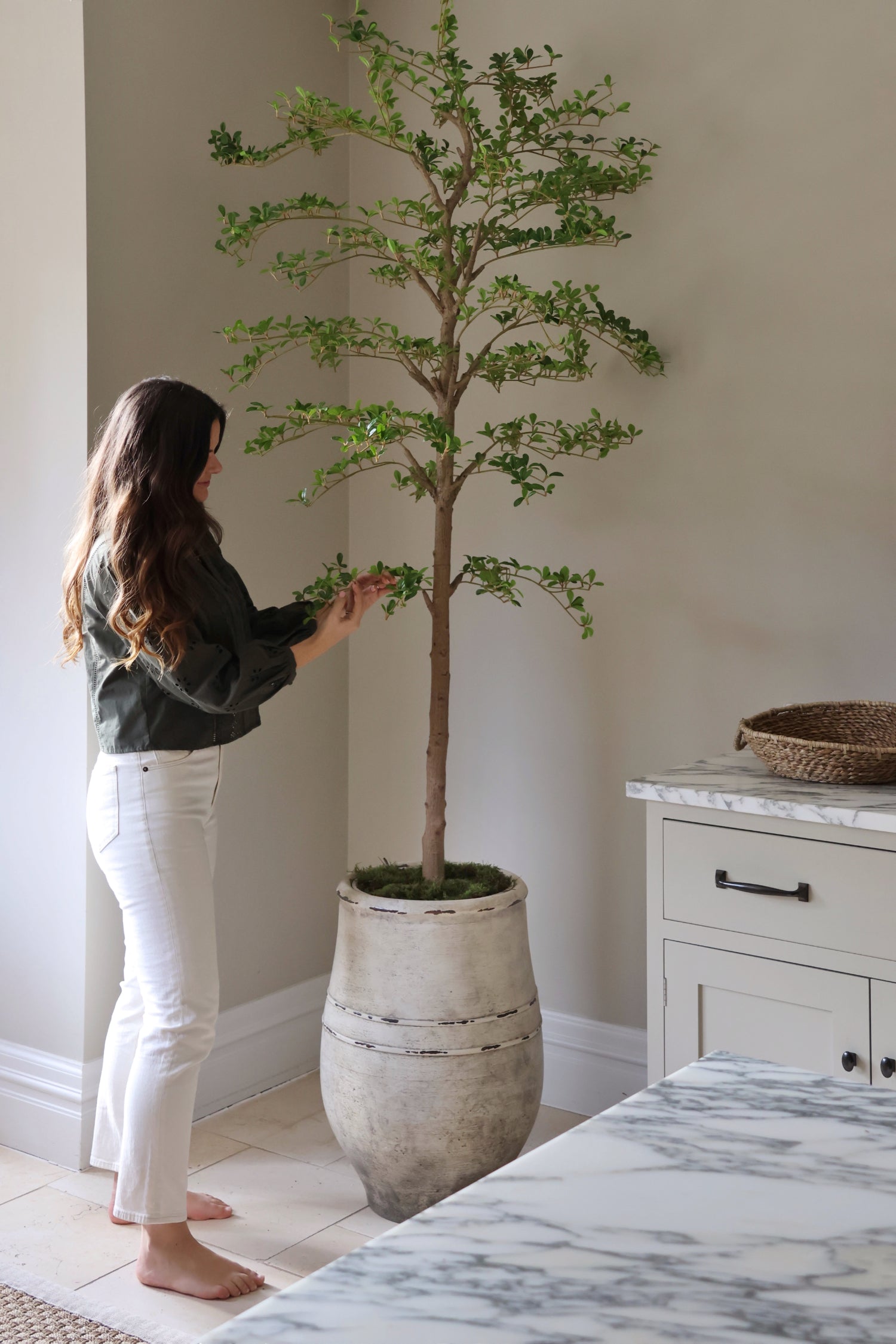 Woman tending to a artificial large tree shady lady in a home setting