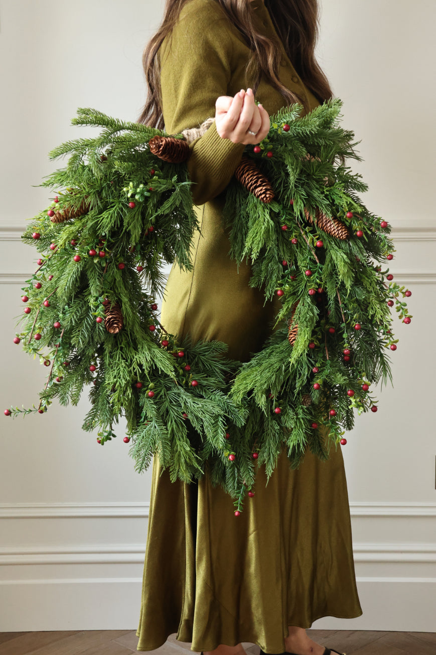 A woman in a green dress holding an artificial christmas wreath with red berries