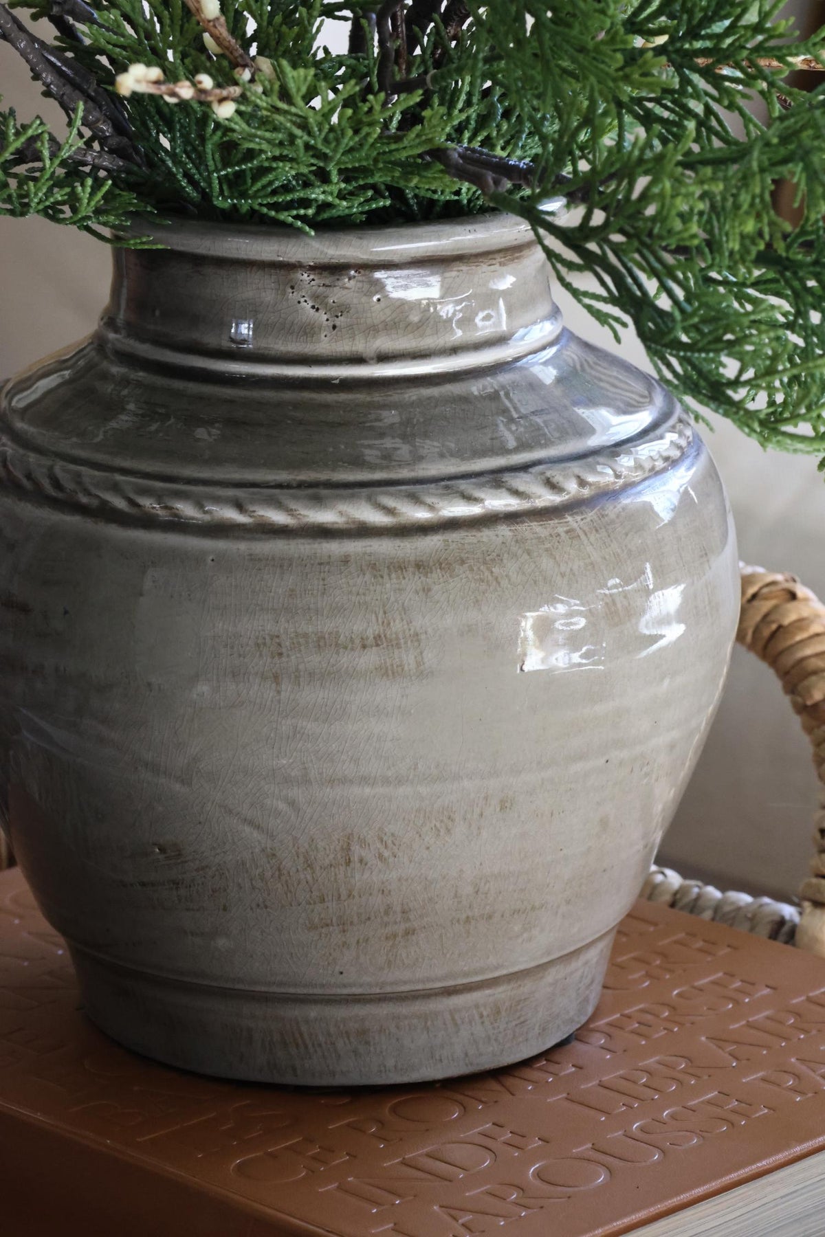 Grey rustice ceramic vase with green foliage in sat on an embossed brown book
