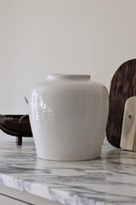 A large, off white ceramic vase with a smooth finish, displayed on a marble surface.