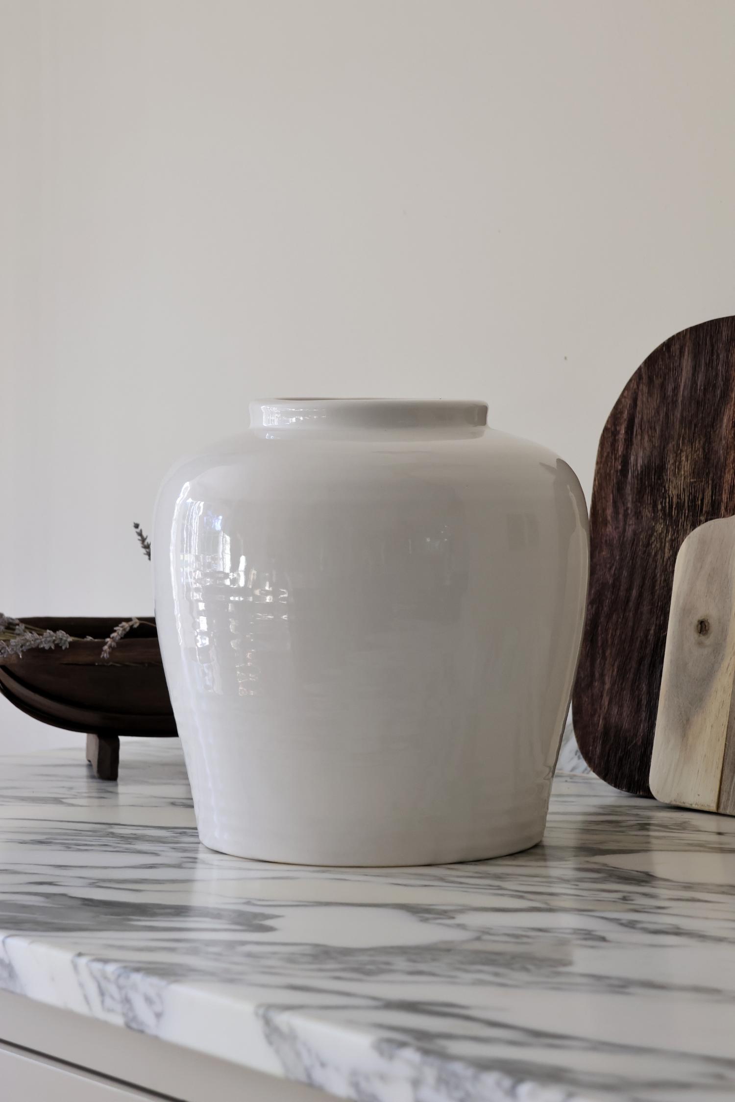 A large, off white ceramic vase with a smooth finish, displayed on a marble surface.