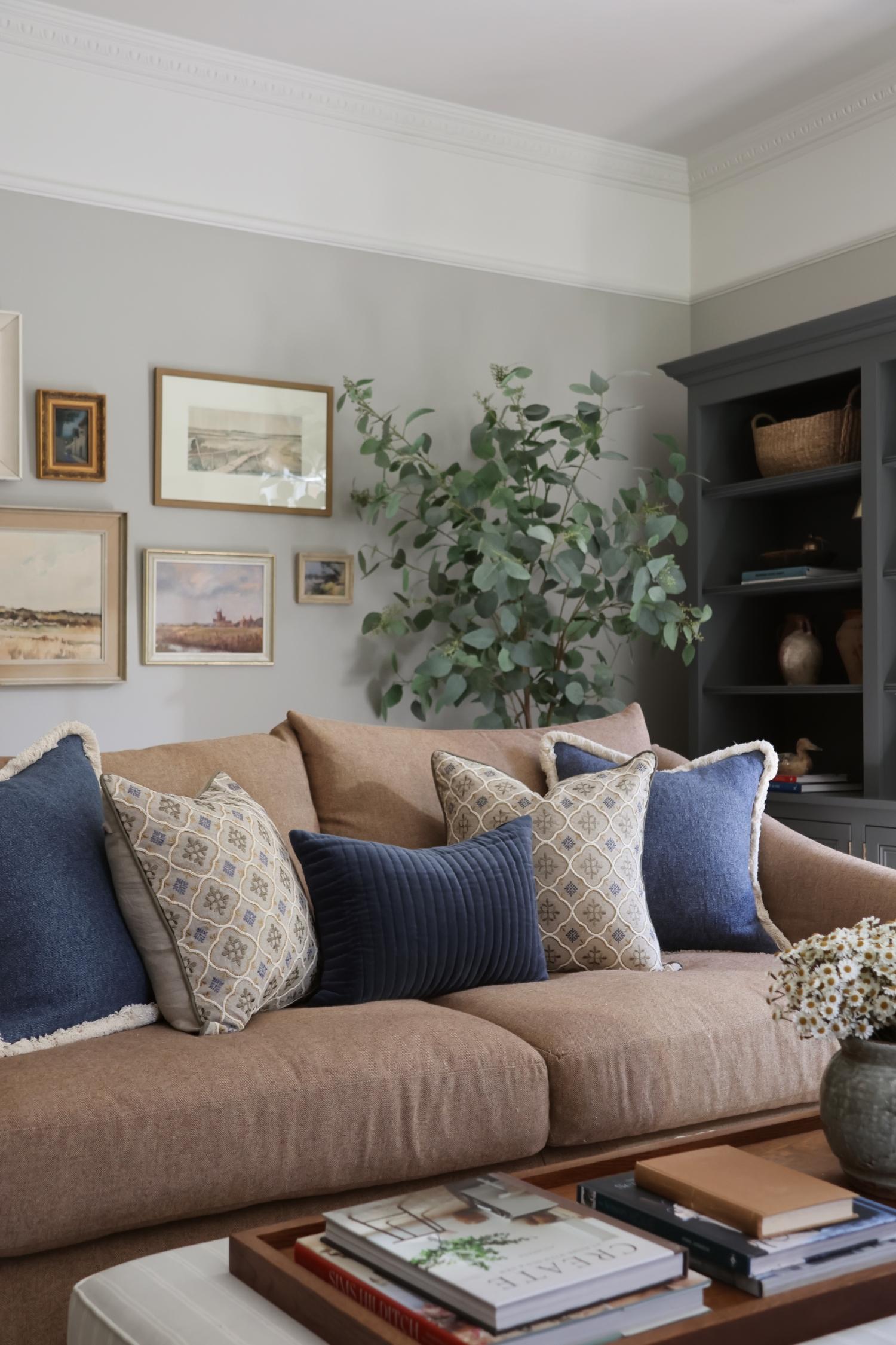 Living room with a beige sofa adorned with blue and patterned decorative cushion, a coffee table with books, and decorative items.