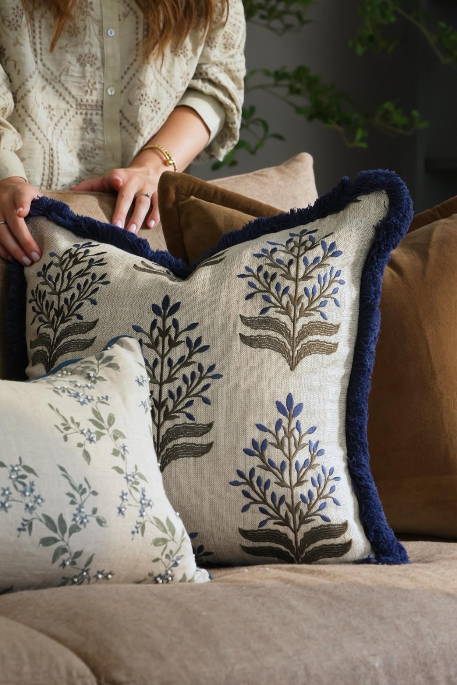 Person holding decorative cushions with floral patterns on a couch.