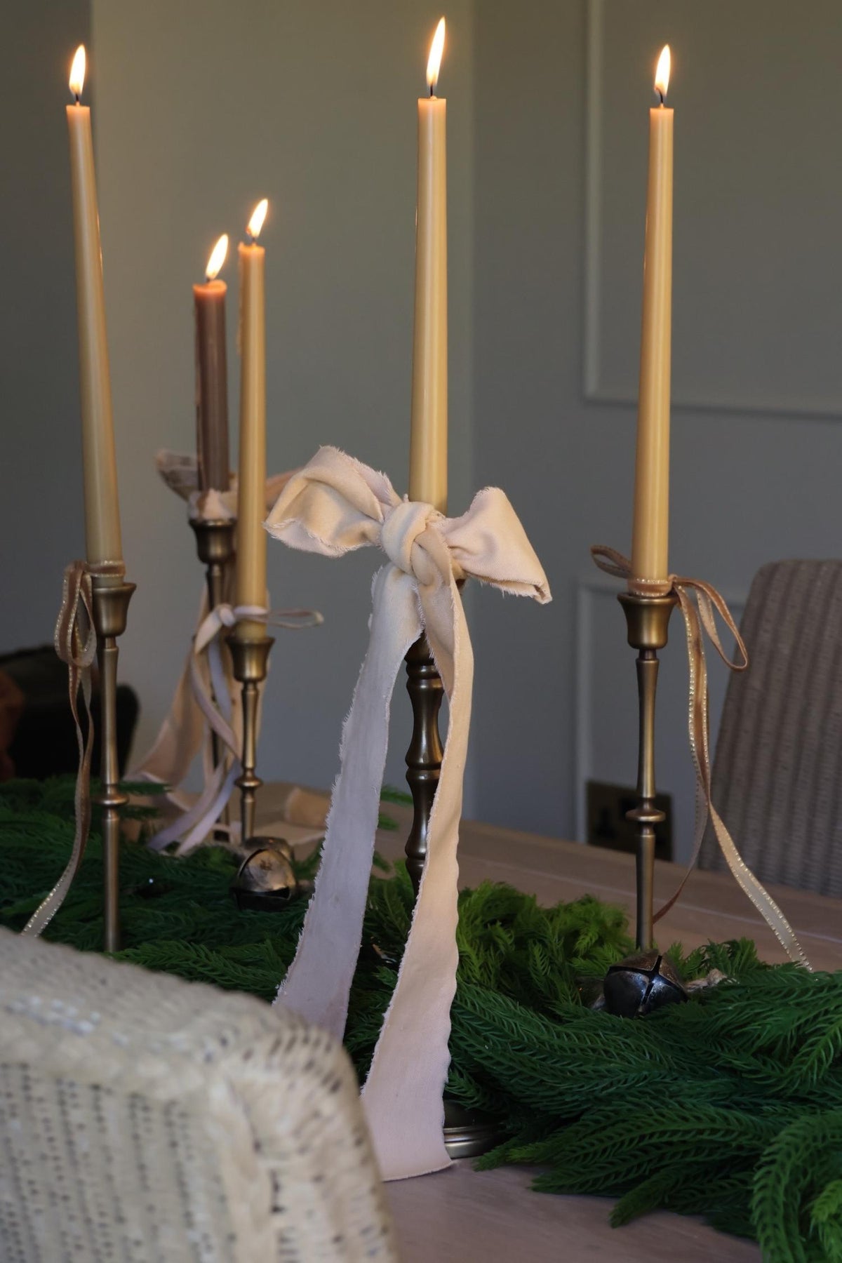 Tall brass candlesticks with ribbon velvet bow tied to the top on a wooden dining table 