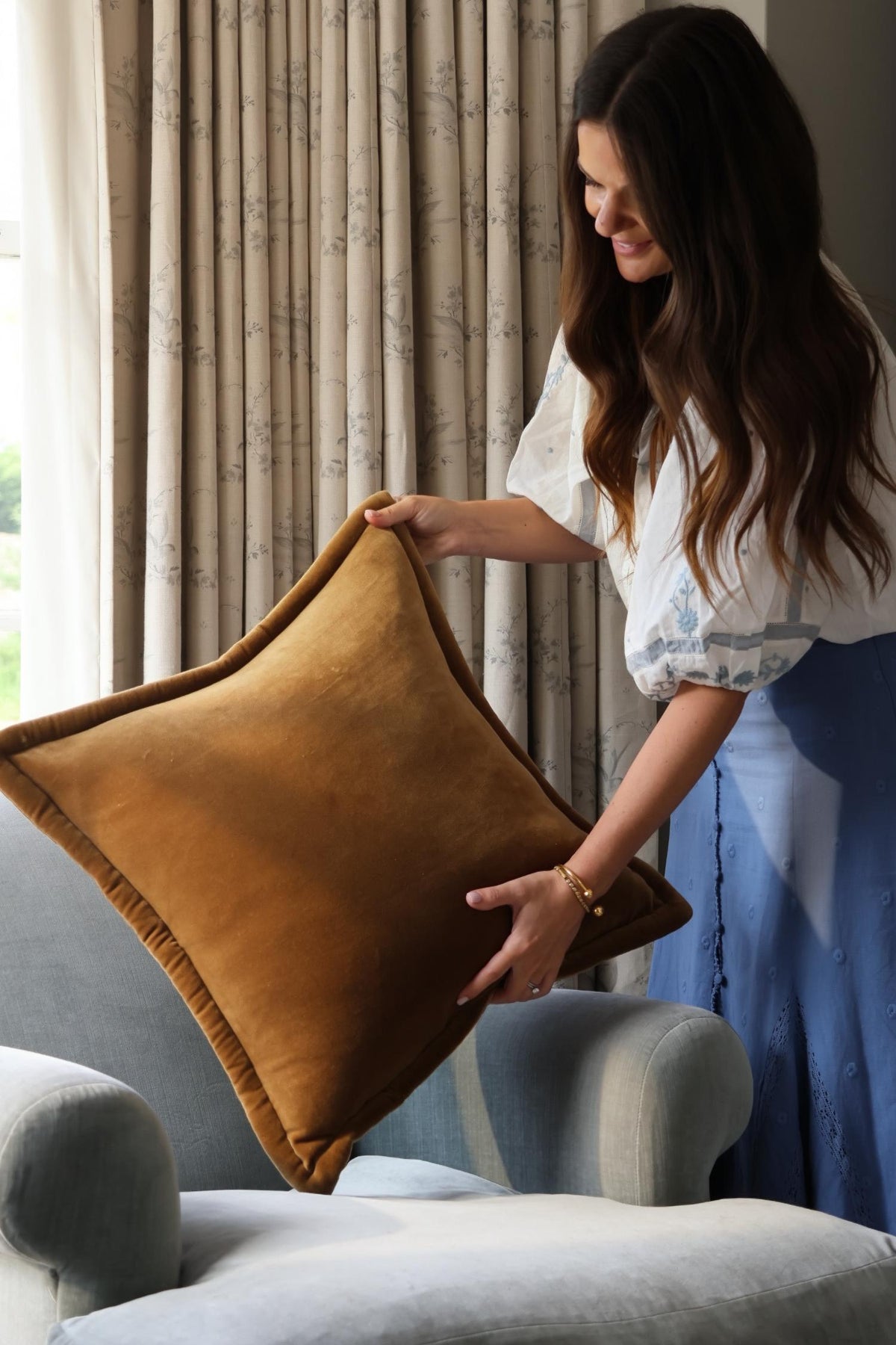 woman putting a large velvet ochre cushion onto a pale blue armchair