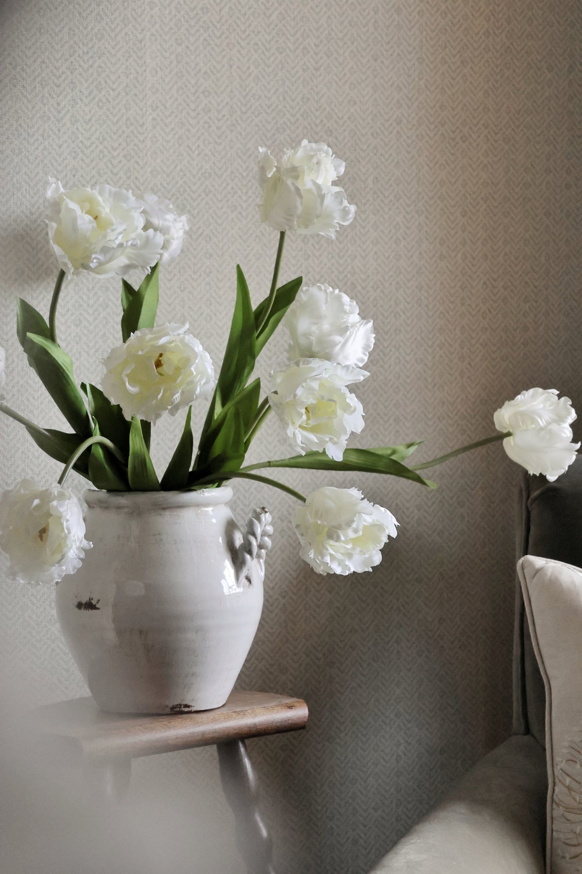 White tulips in a vase on a small table against a neutral wall.