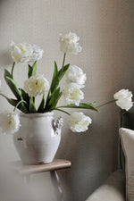 White tulips in a vase on a small table against a neutral wall.