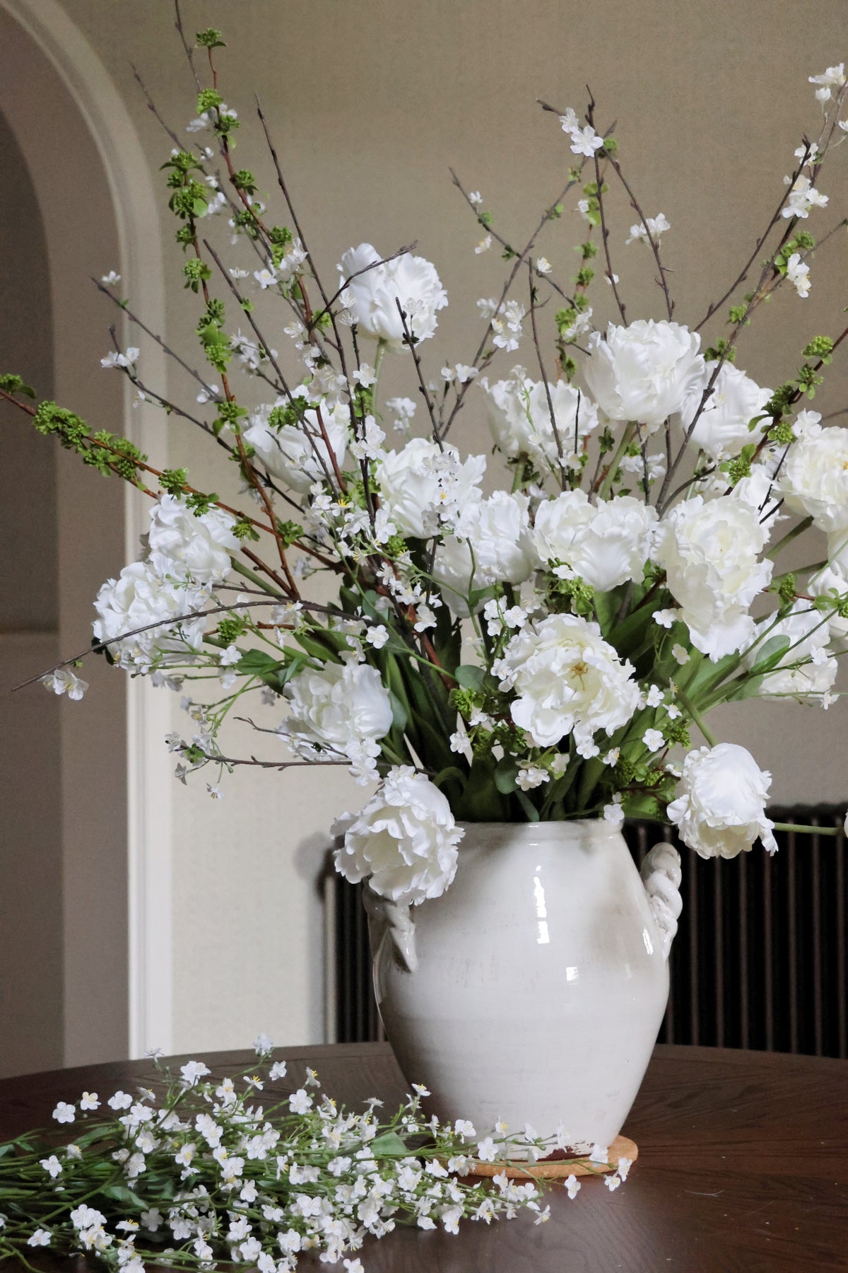 Large white tulip floral arrangement in a vase on a table with a neutral background