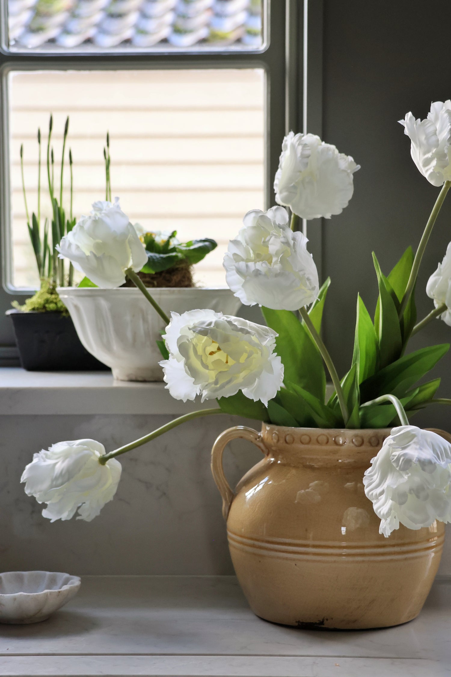 White faux tulips in a yellow vase on a windowsill with a blurred background