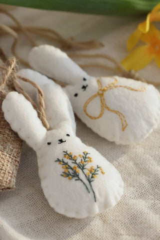 Two white fabric bunnies with embroidered details on a textured surface