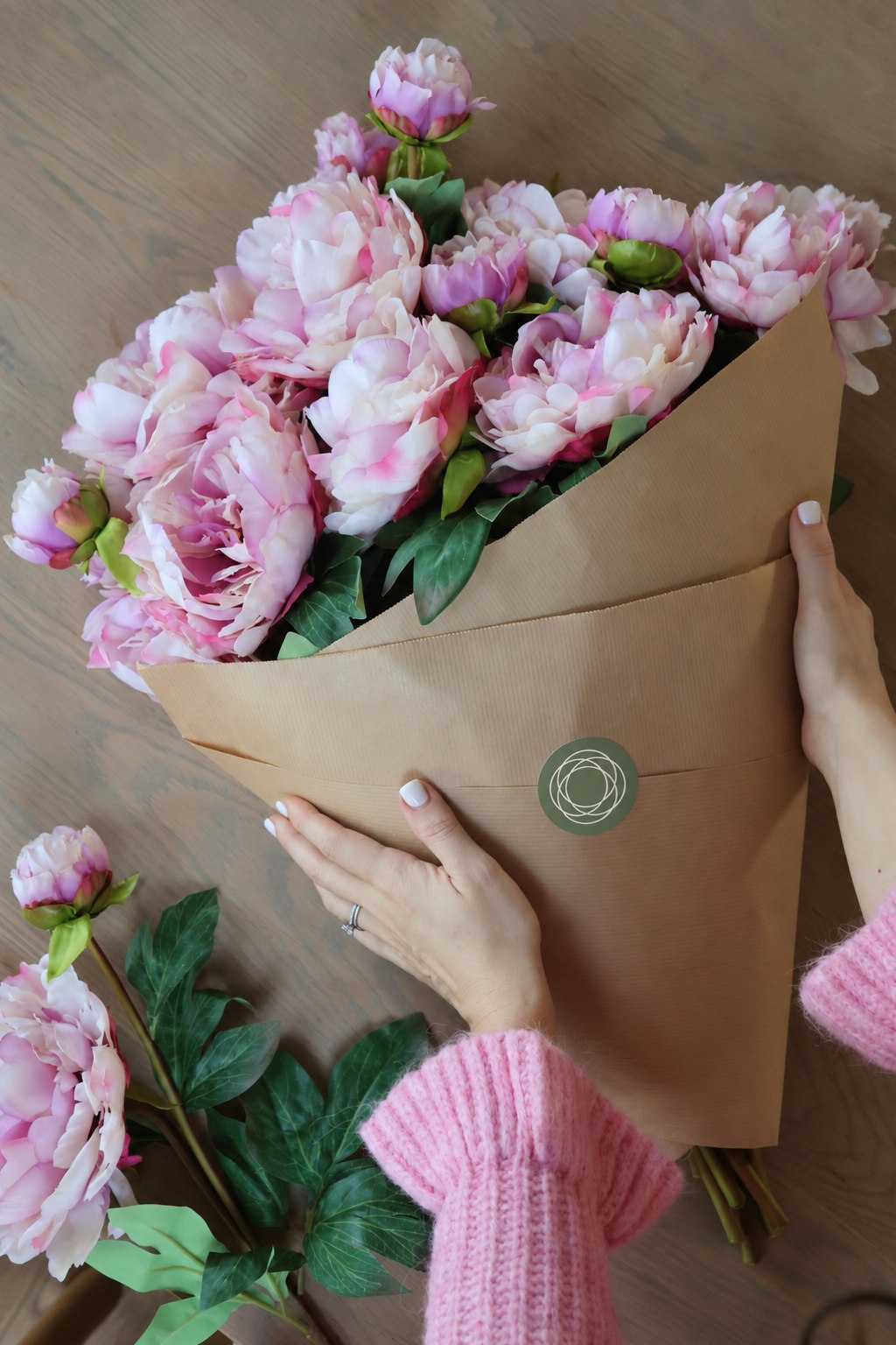Large bouquet of faux blush pink peonies wrapped in brown paper on wooden table