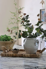 Woven rectangular tray with a vase of eucalyptus on a marble kitchen island 