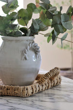 White ceramuc vase with eucalyptus on a woven banana bark tray